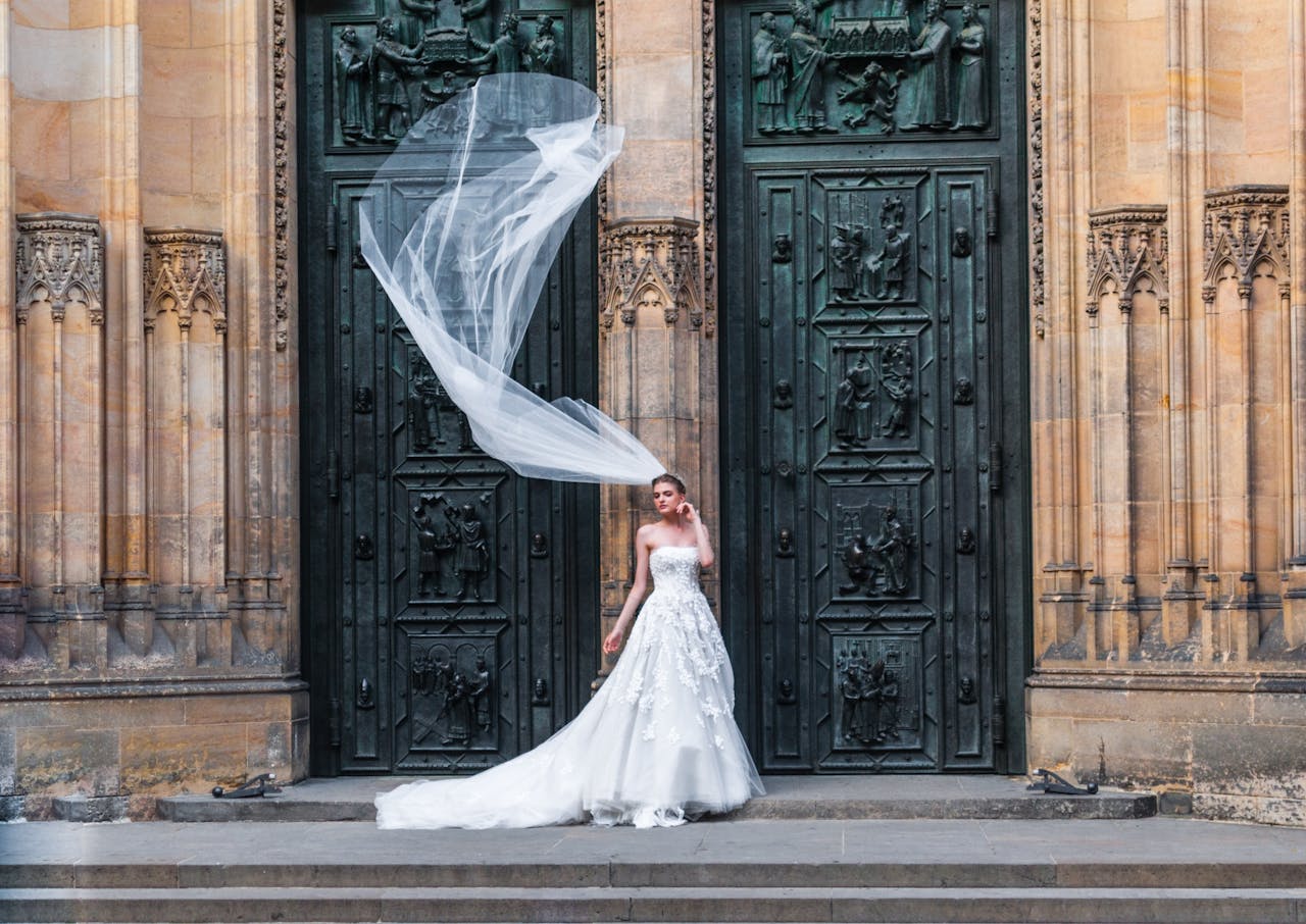 A beautiful bride poses with flowing veil in front of a gothic cathedral entrance.