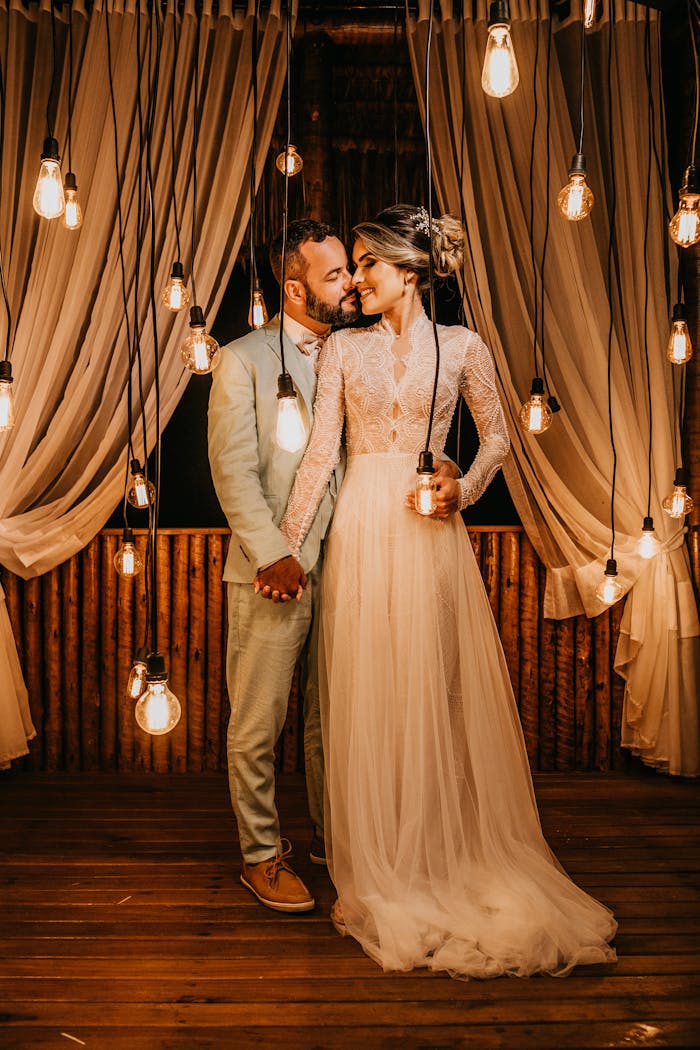Bride and groom hold hands under hanging lights in an elegant indoor setting.