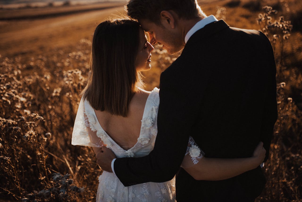 A bride and groom share an intimate moment in a golden field at sunset, symbolizing love and new beginnings.